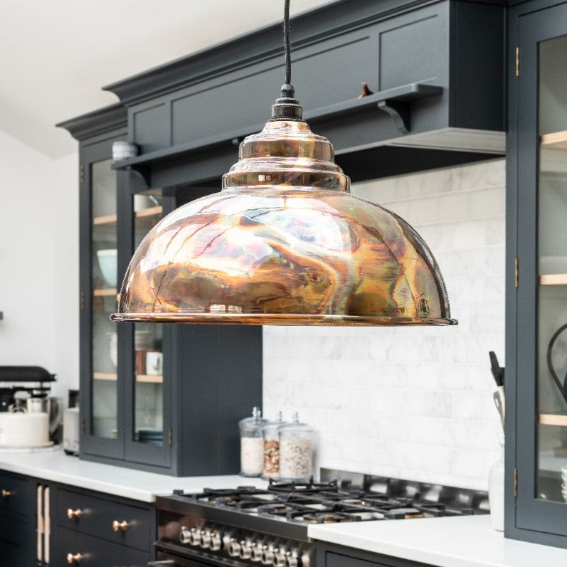Burnished Harborne pendant hanging above a hob in a dark blue kitchen.