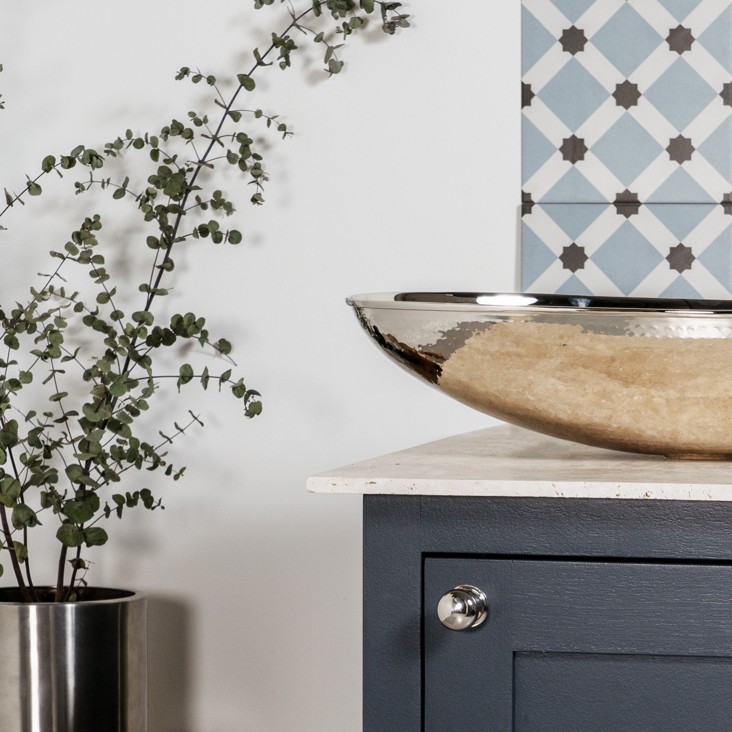 Satin Stainless Steel plant pot, Hammered Nickel sink, and Polished Chrome From The Anvil cabinet knob in a blue tiled bathroom.