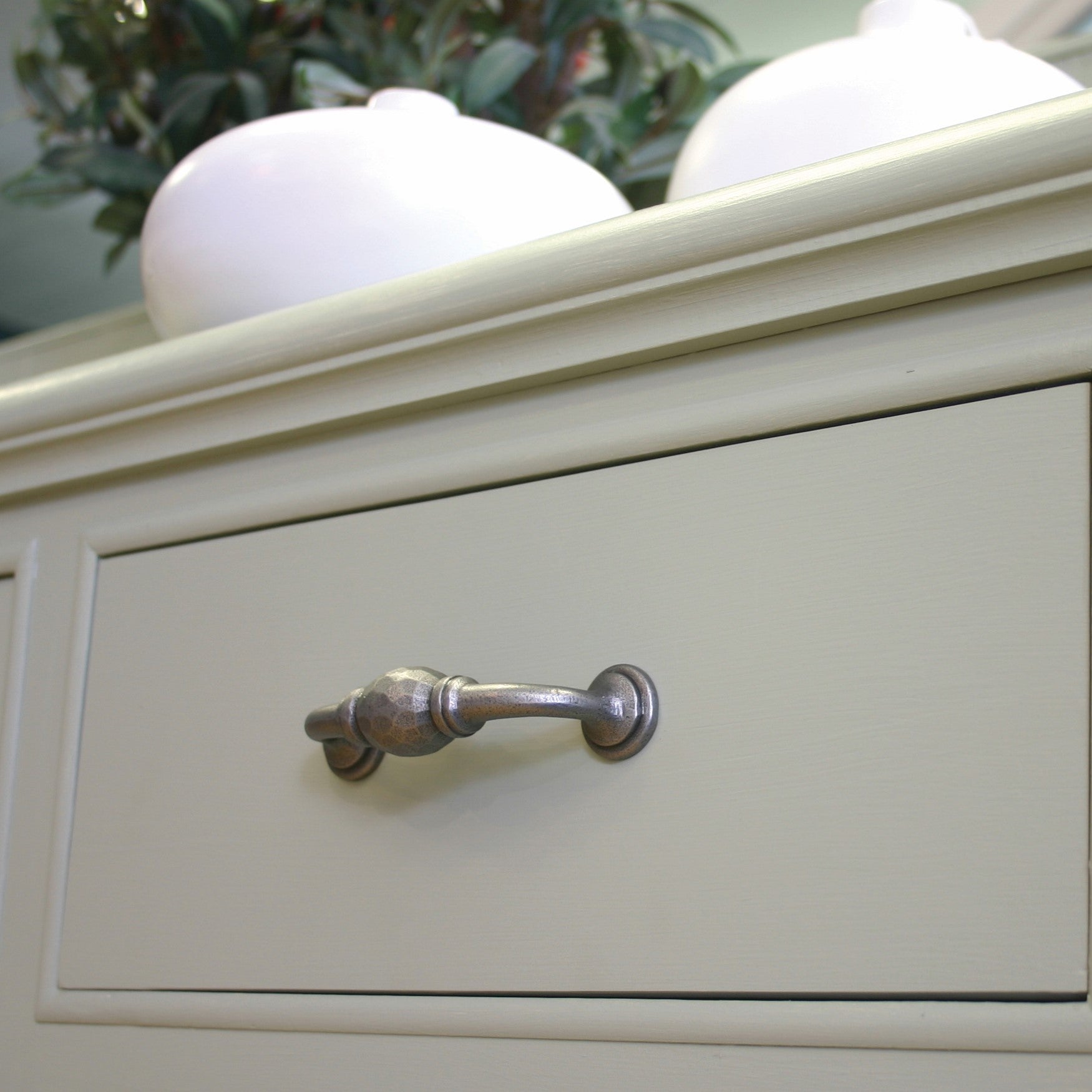 Decorative Pewter pull handle on a grey-green drawer with two white bowls on top of the unit and a green plant in the background.