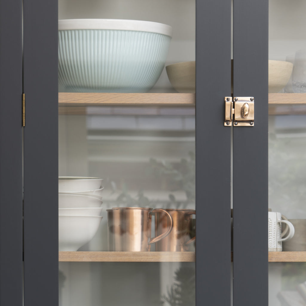 From The Anvil's Polished Bronze cabinet lock on a dark blue glazed cabinet filled with kitchenware.