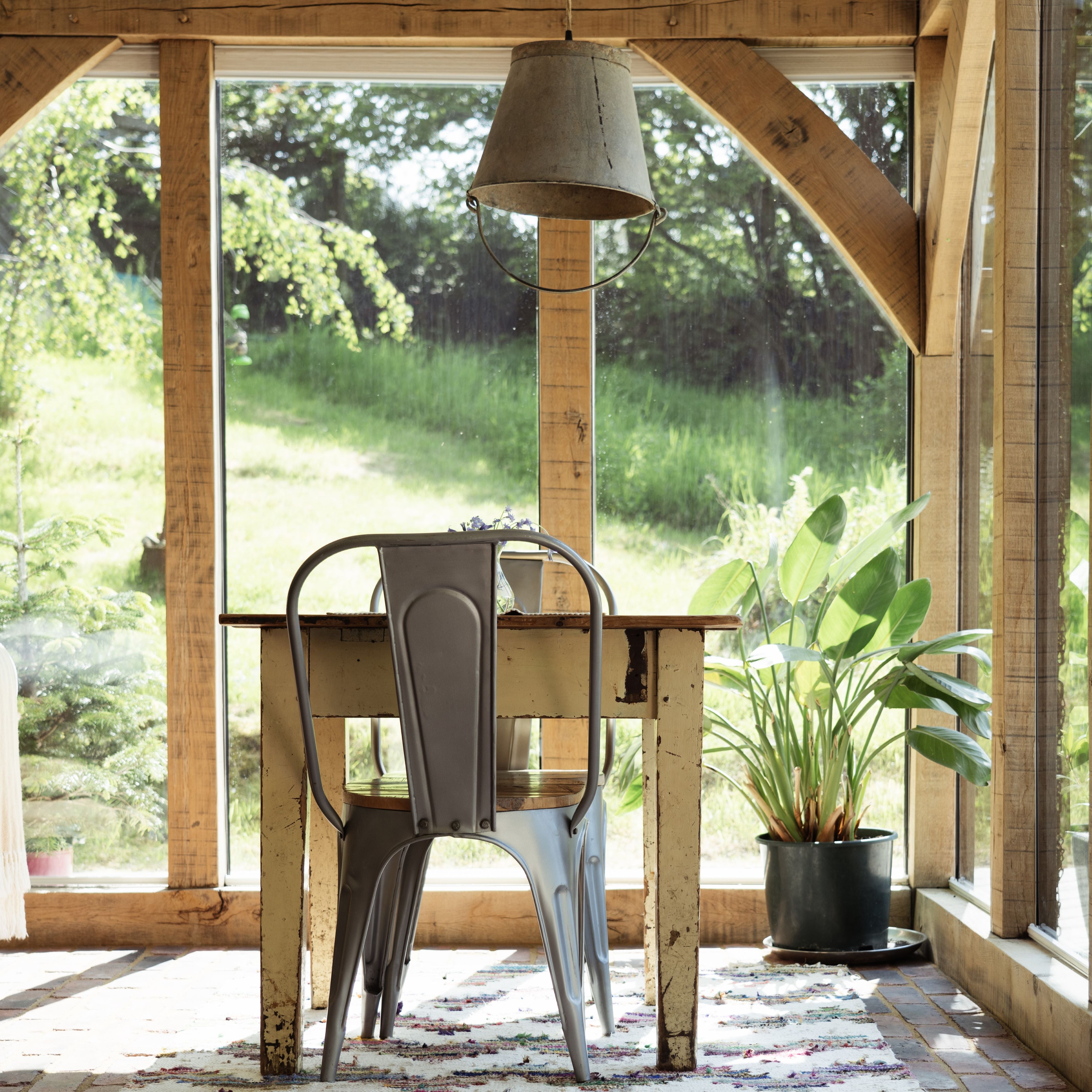 Rustic wooden dining room interior with metal chair, wooden table, metal light pendant, and potted plant.