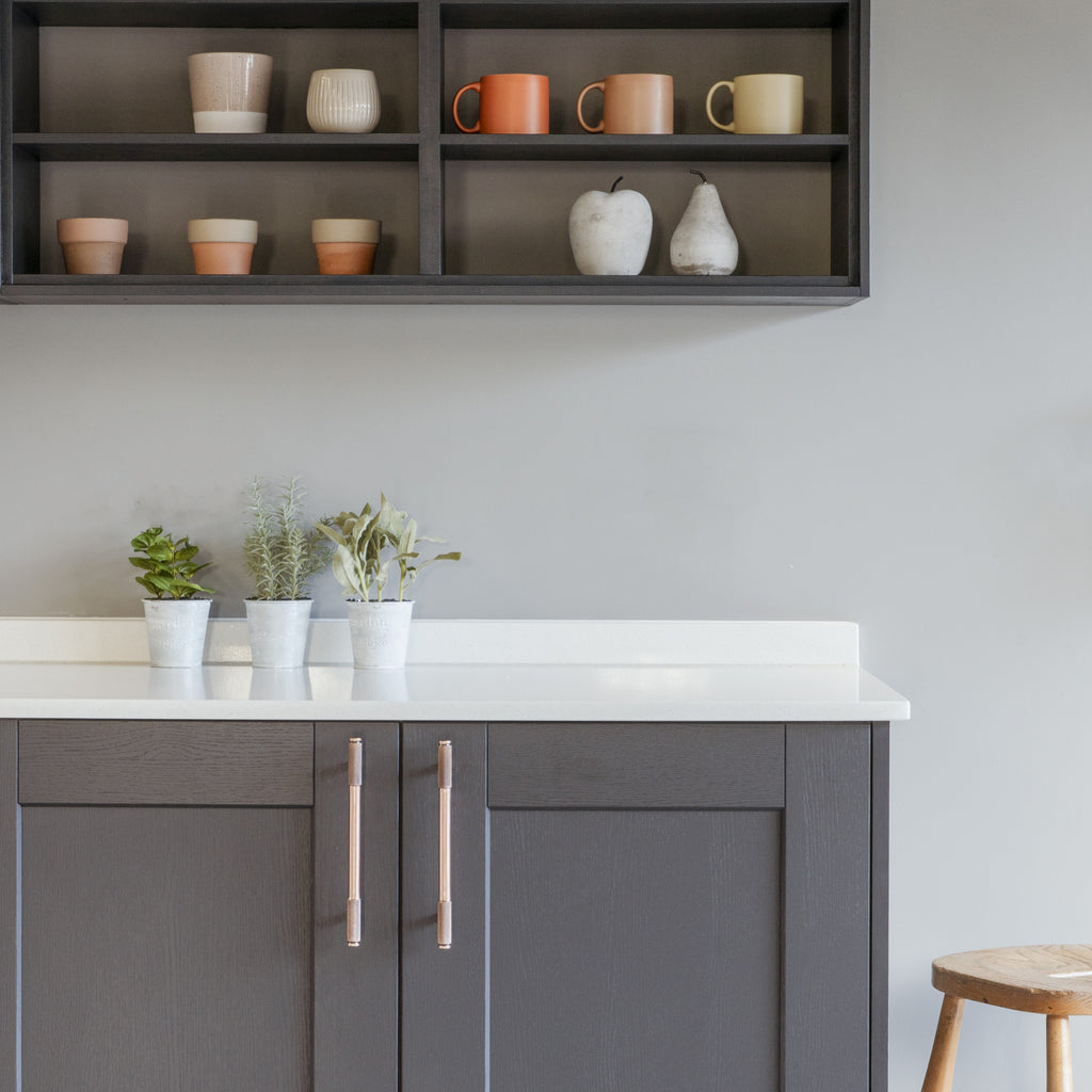 Grey kitchen cabinets with From The Anvil Brompton pull handles, with a grey shelf above with ceramic mugs.