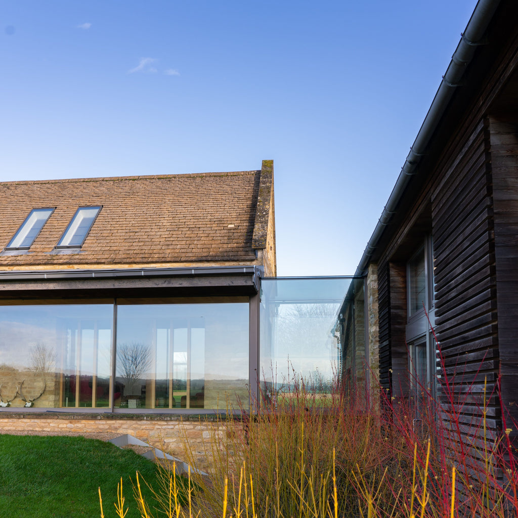 Modern barn conversion with a large glass walkway connecting to a wooden building.