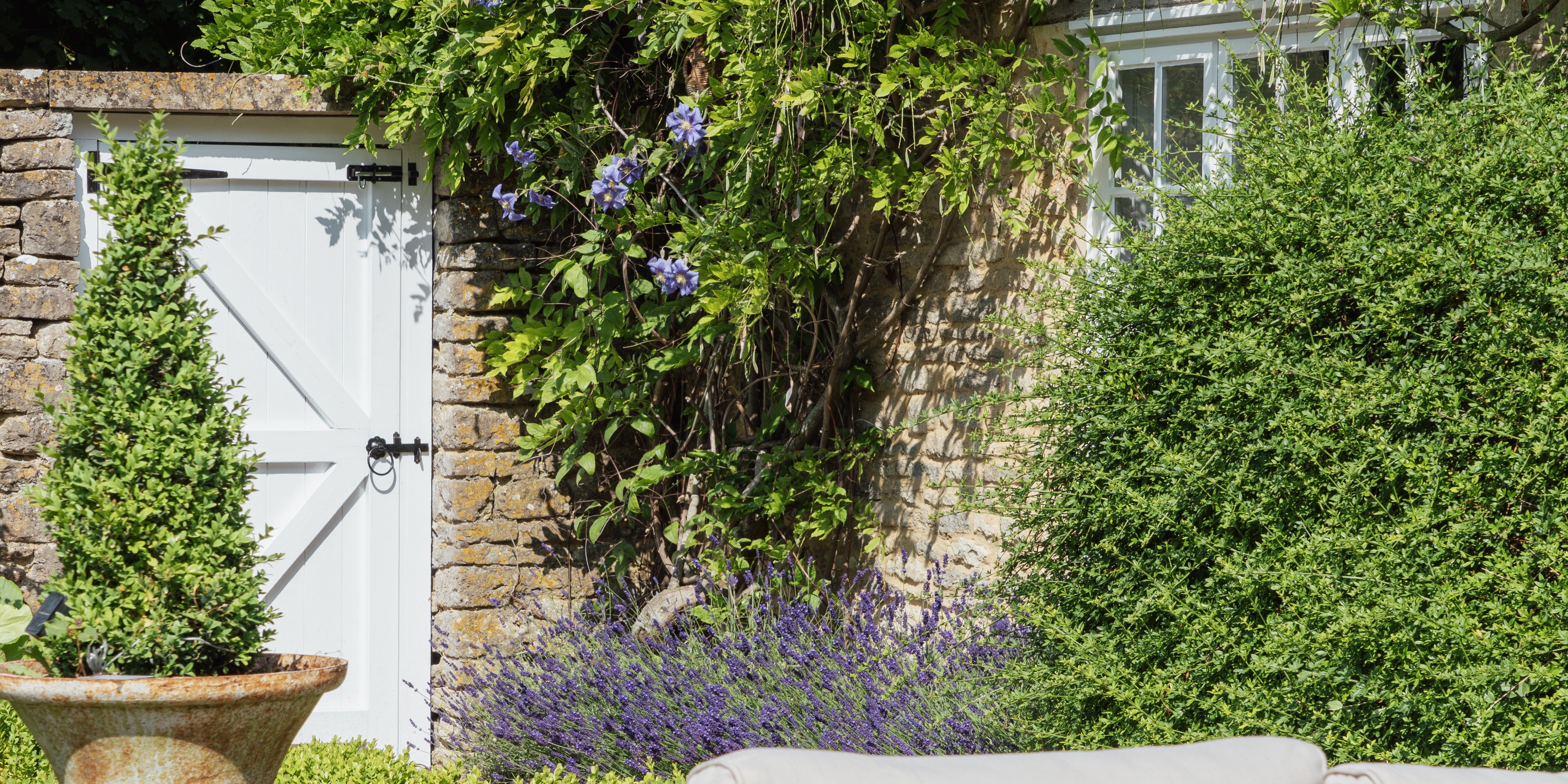 White external door with a Black From The Anvil Cottage latch in a green garden.