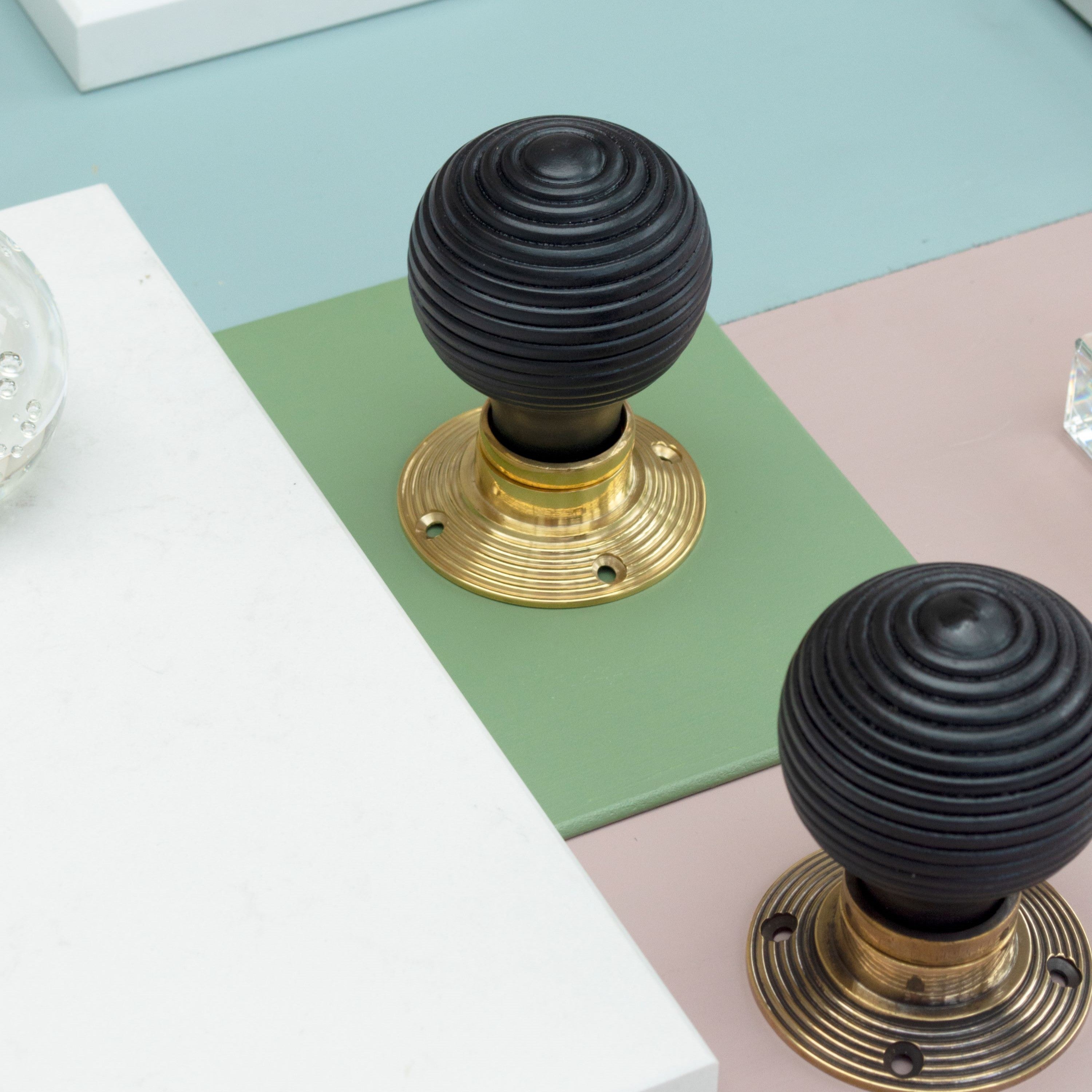 Ironmongery mood board with green, blue, white and pink background, featuring two Ebony door handles with Brass roses.