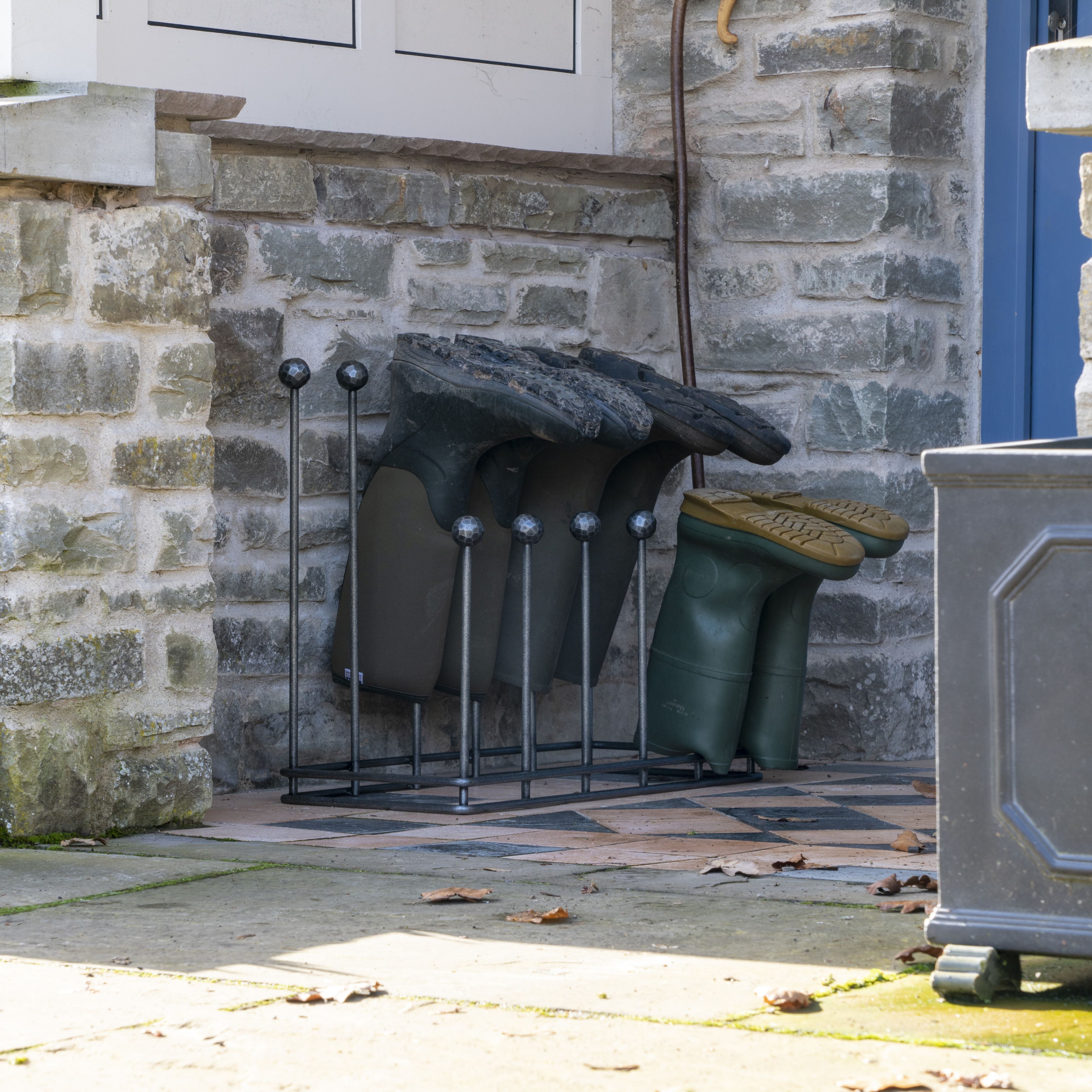 From The Anvil Pewter boot rack filled with welly boots, outside a backdoor.