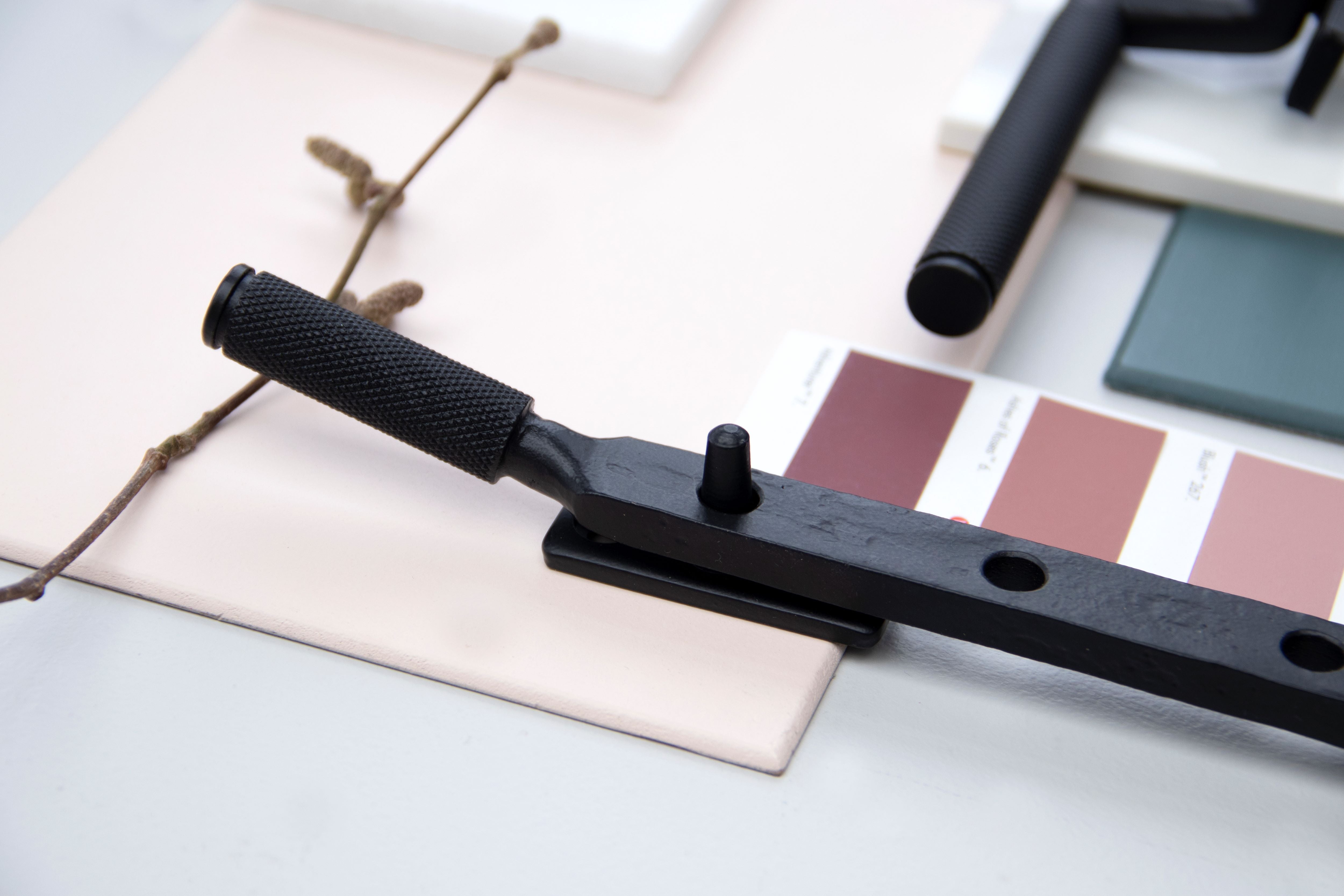Matt Black knurled window hardware on pink paint swatch with dried twig next to it.