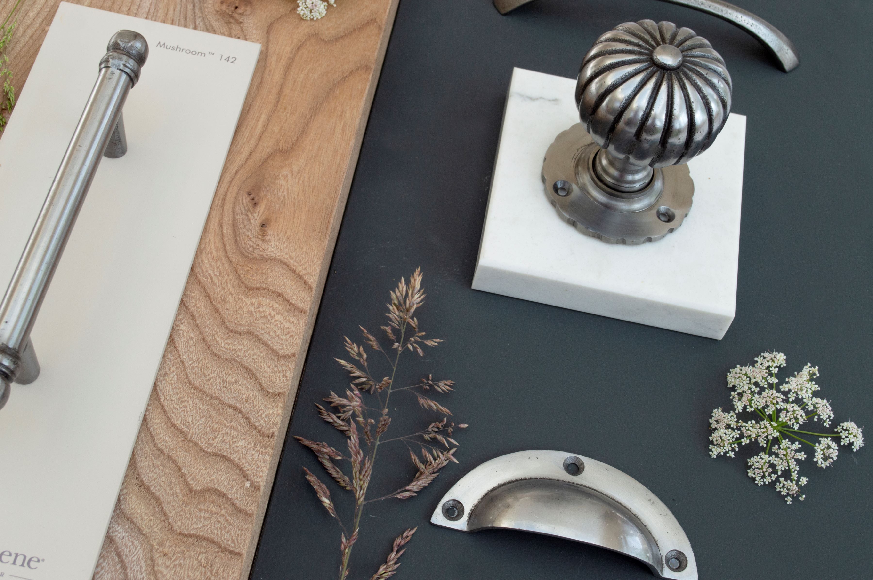 Ironmongery mood board with navy background, wooden slab, dried flowers, and pewter pull handle, drawer pull and cabinet knob.