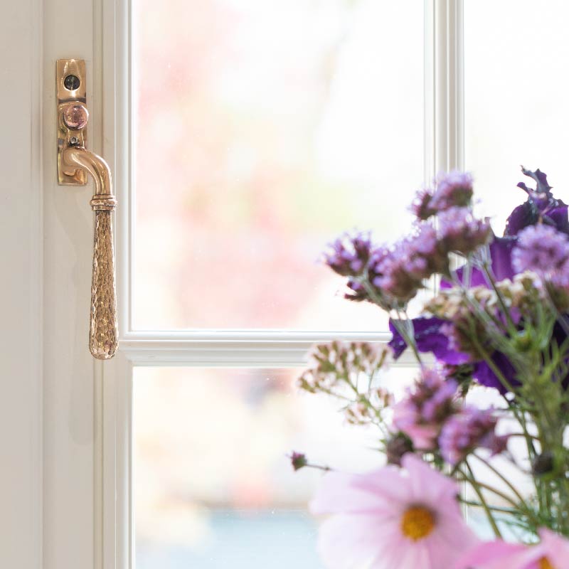From The Anvil Polished Bronze Hammered Newbury window handle on a white uPVC window