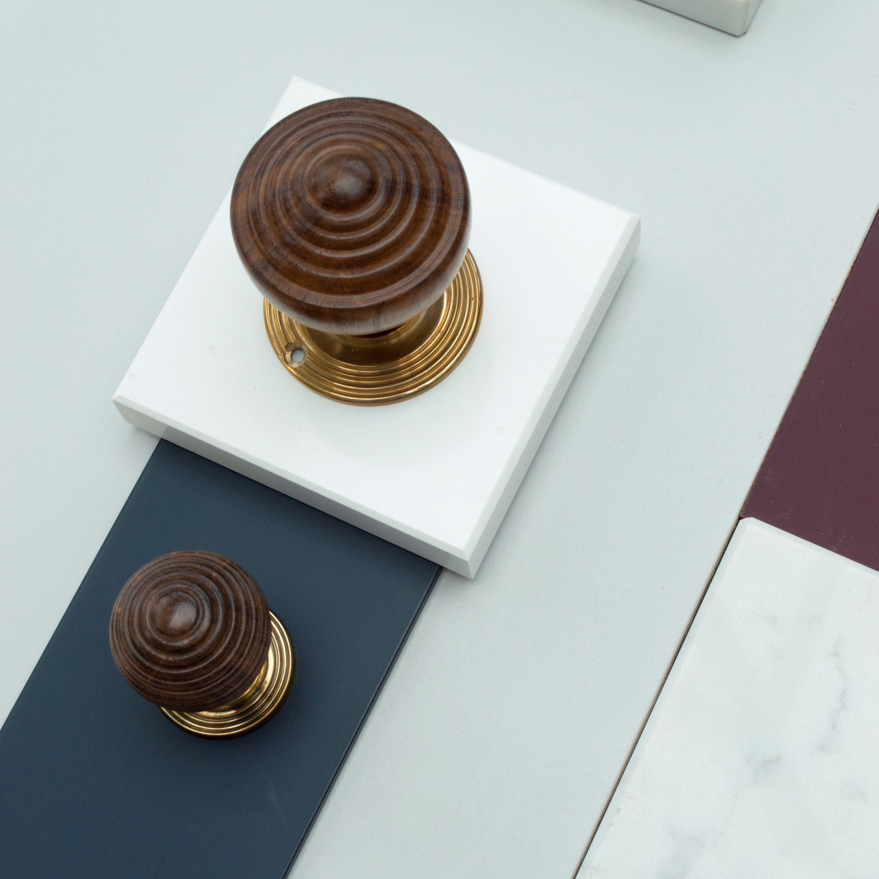 Rosewood and brass cabinet and door handles on a navy blue paint swatch and a piece of white marble, with another square of white marble in the bottom right corner.