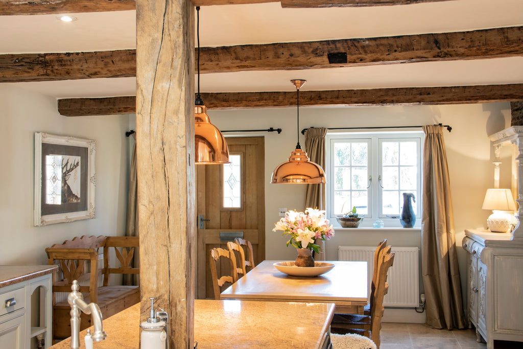 Oak beam cottage interior with Smooth Copper Harborne ceiling pendant lights hung over a dining table.