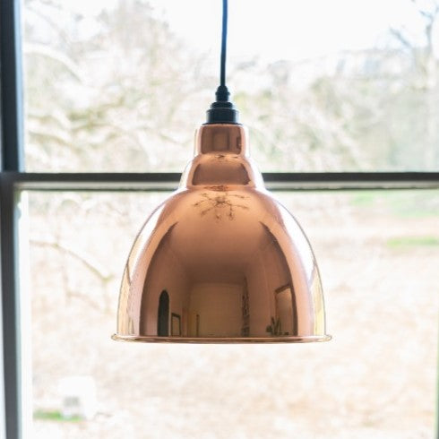 Smooth Copper Brindley pendant with a black cable hanging in front of a window.