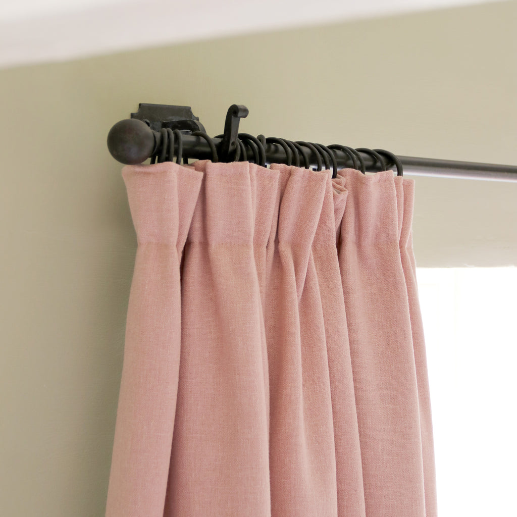 Close-up of a pink pleated curtain on a Beeswax curtain pole with Ball finials against a cream wall.
