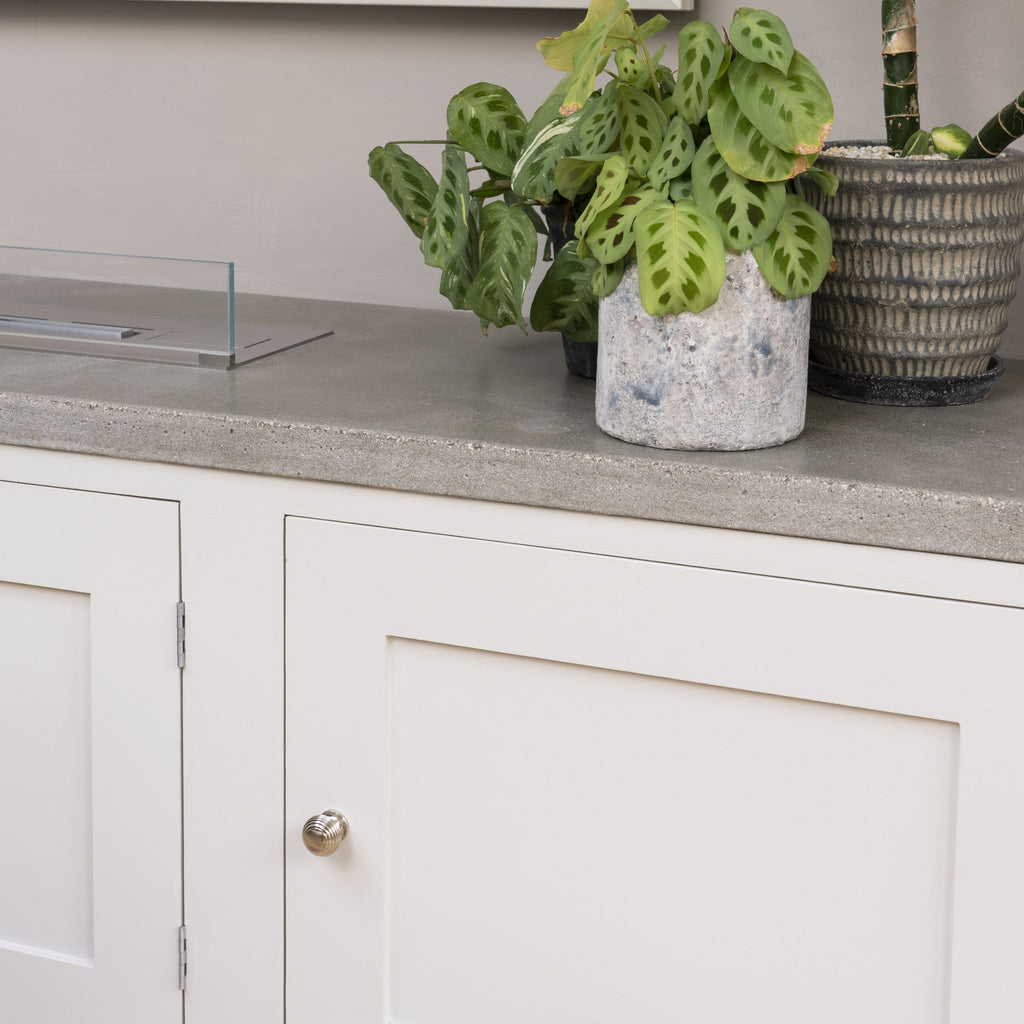 Chrome Beehvie cabinet knob on a cream cabinet with a stone worktop with plants in stone and ceramic pots.