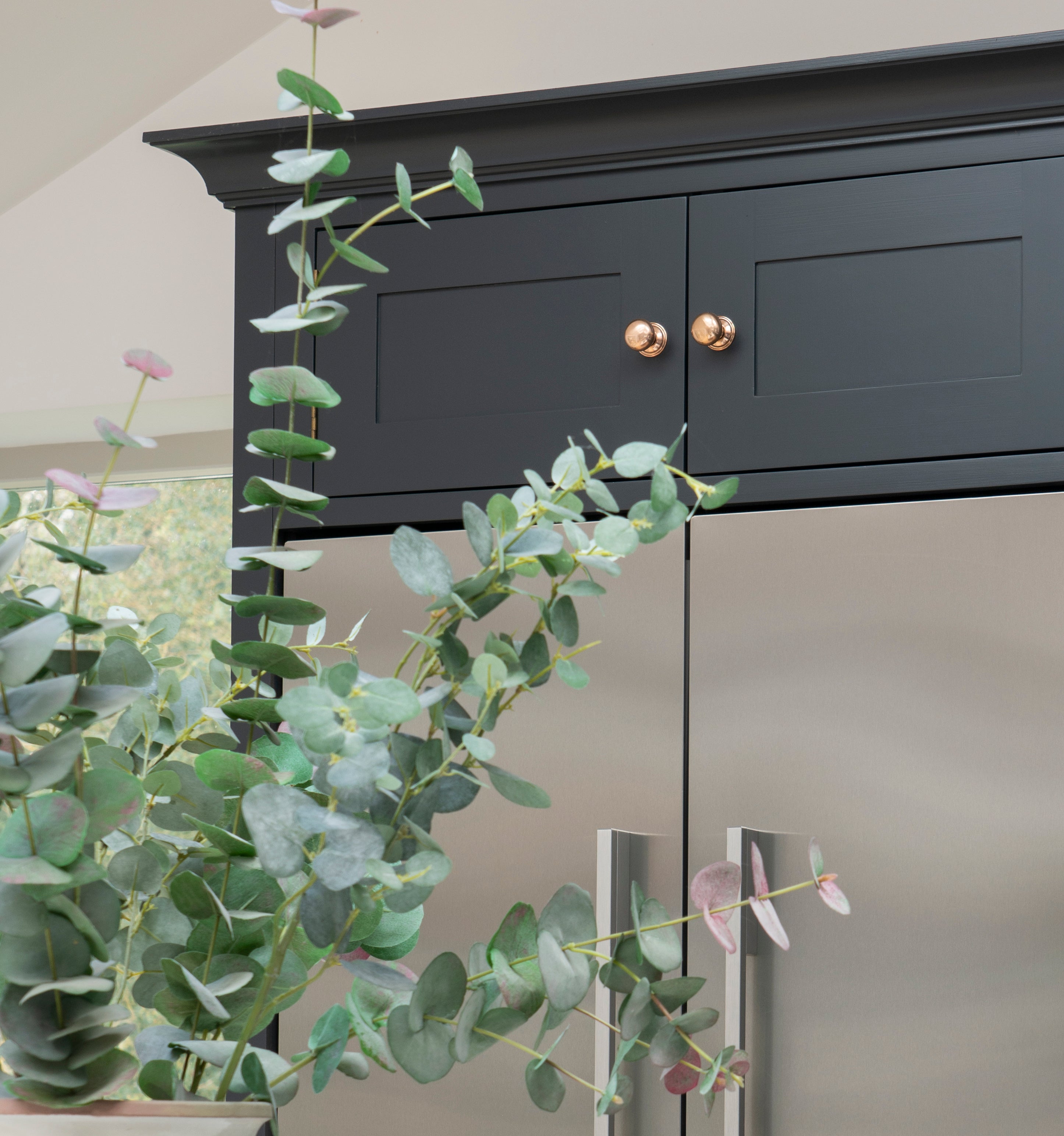 From The Anvil's Polished Bronze cabinet knobs on dark blue cabinets above a stainless steel fridge.