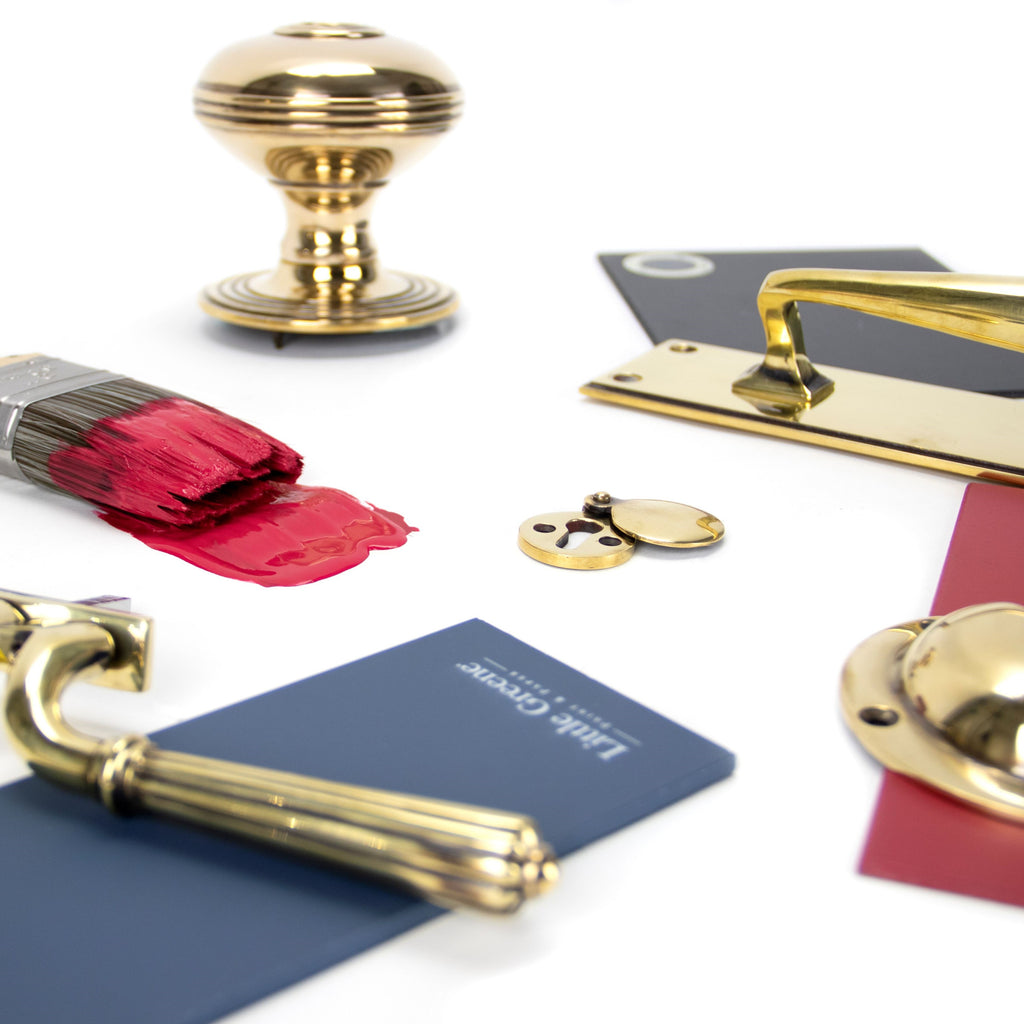 Ironmongery moodboard with Aged Brass window hardware, door knob, escutcheon and pull handles, with navy blue, red and grey paint swatches, plus a paintbrush covered in red paint.