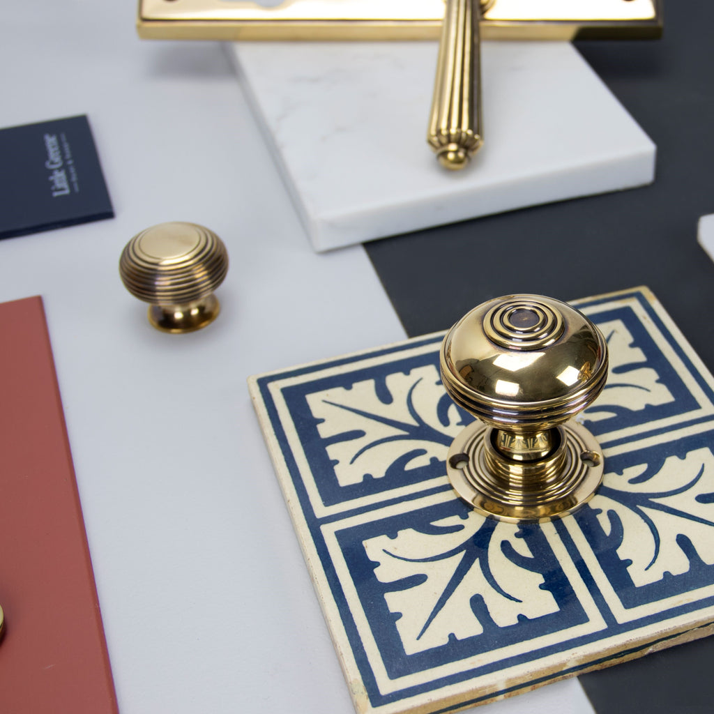 Ironmongery mood board with Aged Brass cabinet knob, door handle & knob, on patterned blue ceramic tile, slab of marble, and red and navy blue