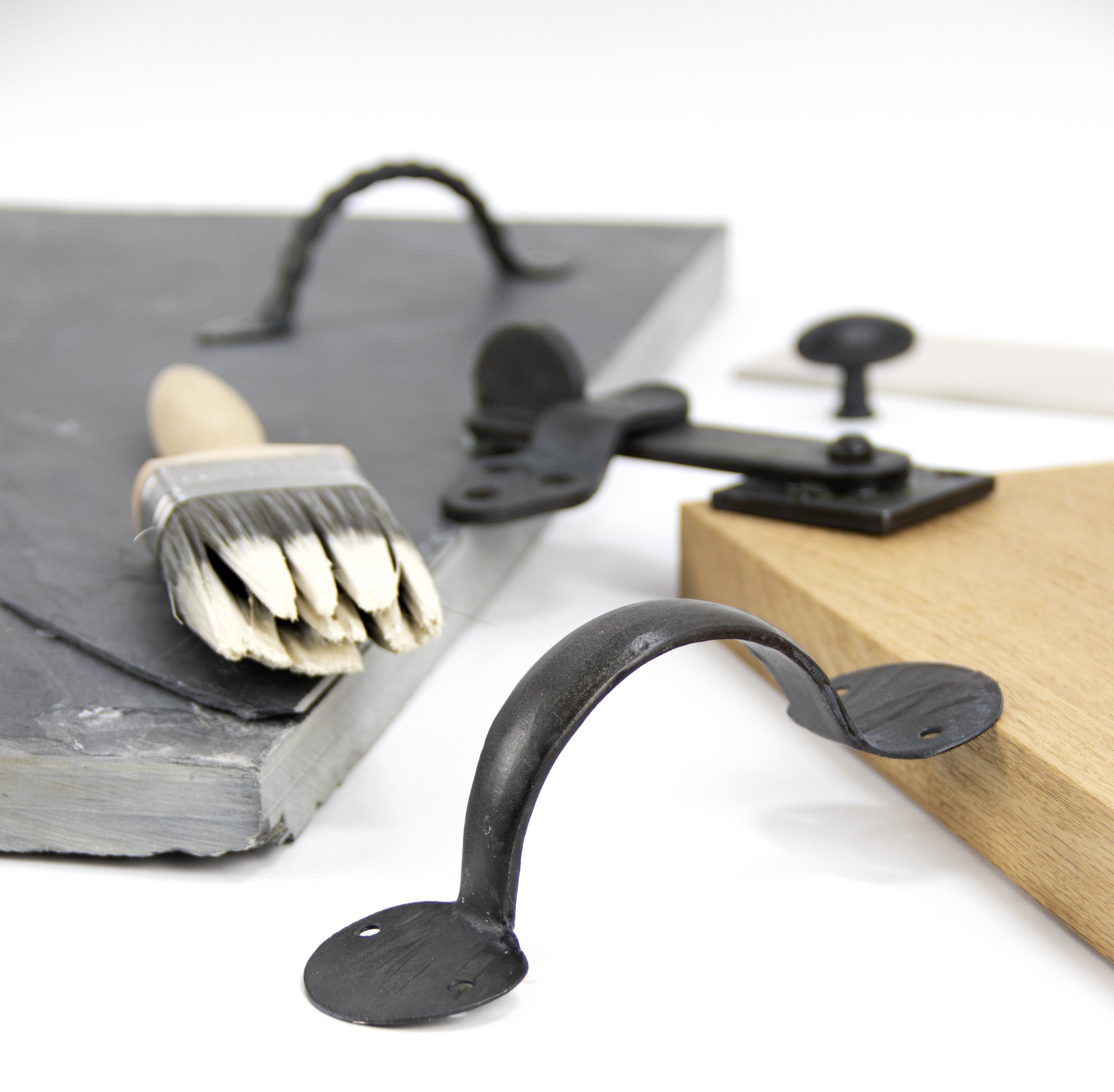 Ironmongery mood board with sheets of slate and wood, featuring our Beeswax pull handles and latch, next to a wooden paint brush with Farrow & Ball paint on it.
