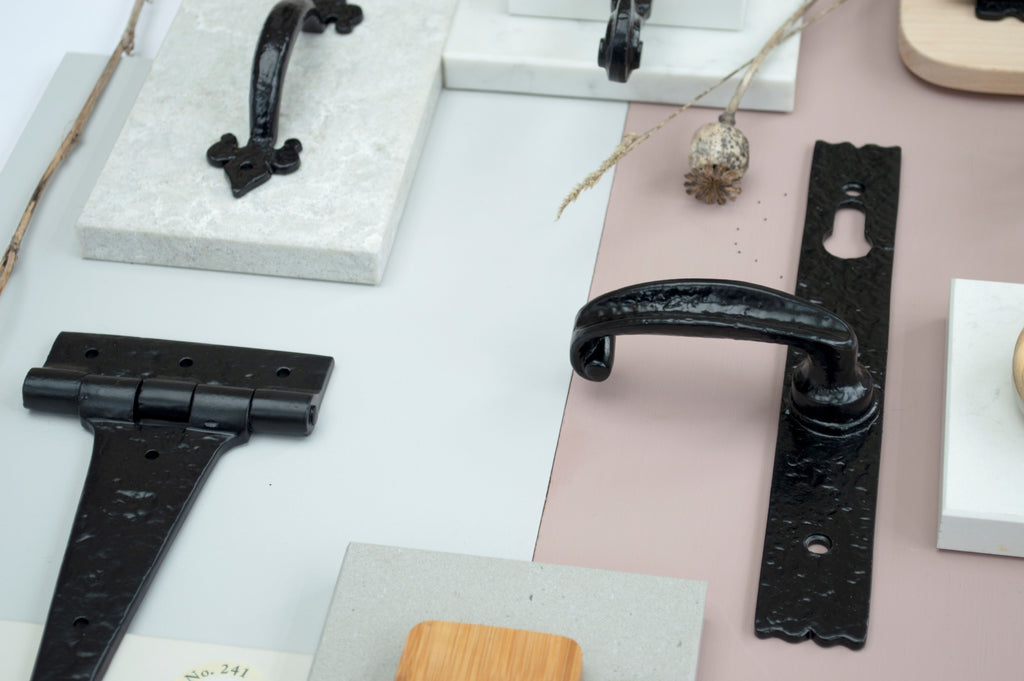 Ironmongery mood board featuring our Black door handles, T hinges and pull handles on different slabs of marble and coloured paint swatches.