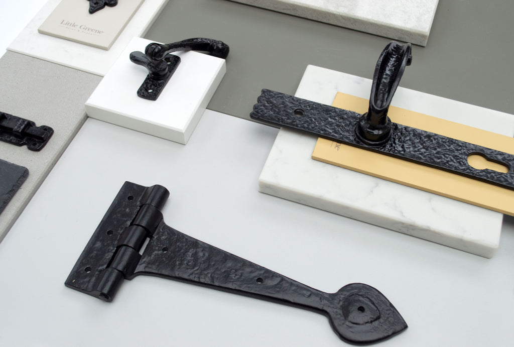 Ironmongery moodboard on a white background featuring black T hinges, door handles and window hardware on slabs of marble and swatches of paint.