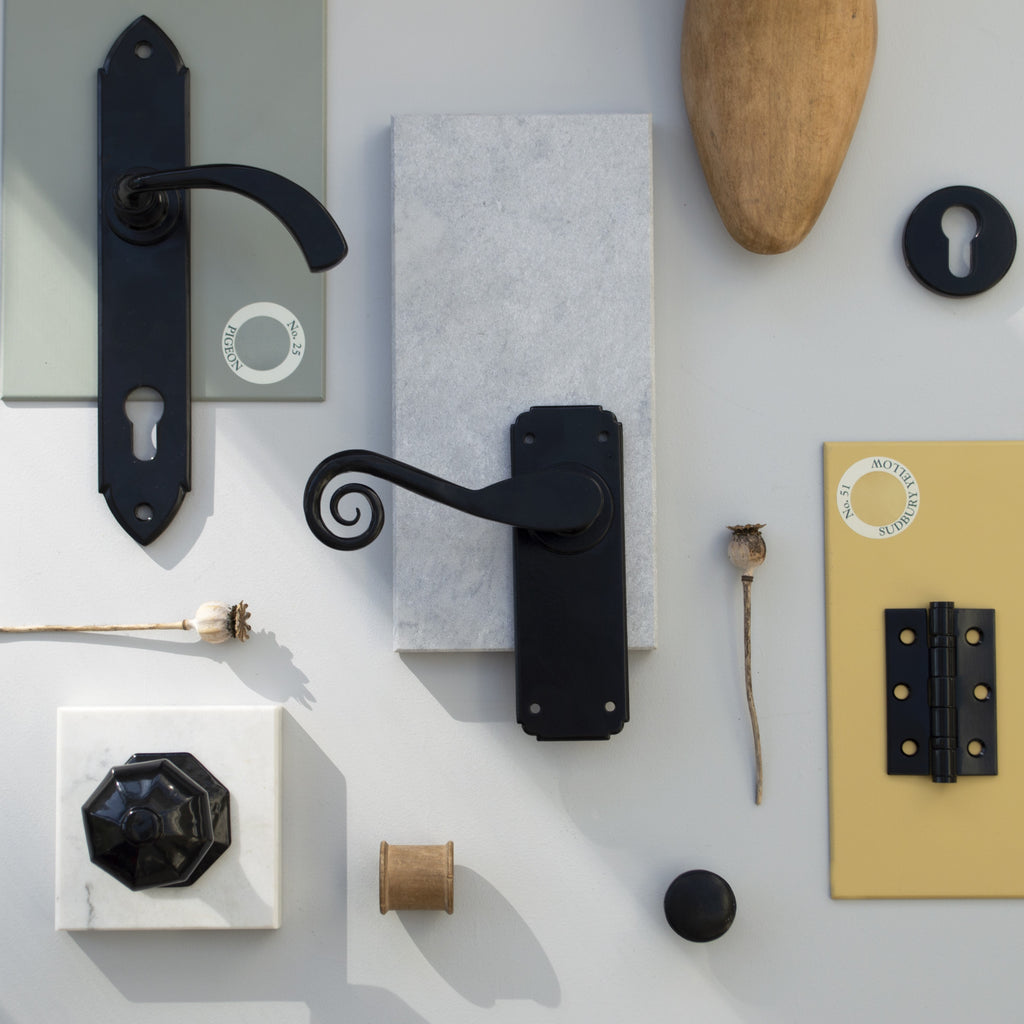 An ironmongery moodboard on a white background, featuring our Black door handles, hinges, escutcheon, cabinet knob and door knob with green & yellow paint swatches, slabs of marble and natural décor.
