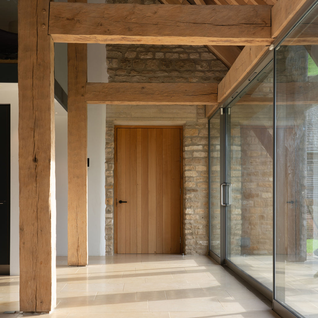 Contemporary hallway with glass walls and oak beams in a barn conversion with wooden panelled doors with From The Anvil Matt Black lever on rose door handles.