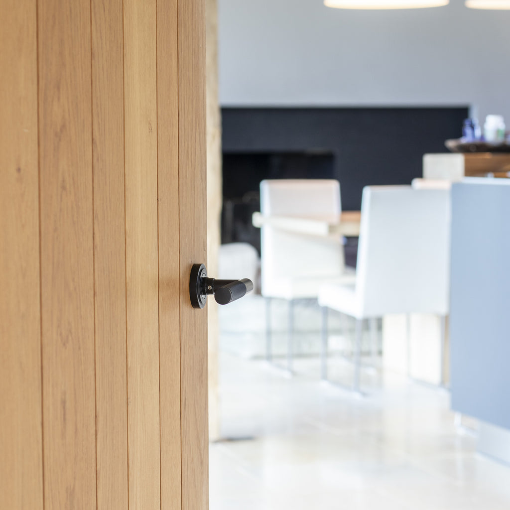 Wooden door with a From The Anvil knurled Black door handle leading into a modern dining room.