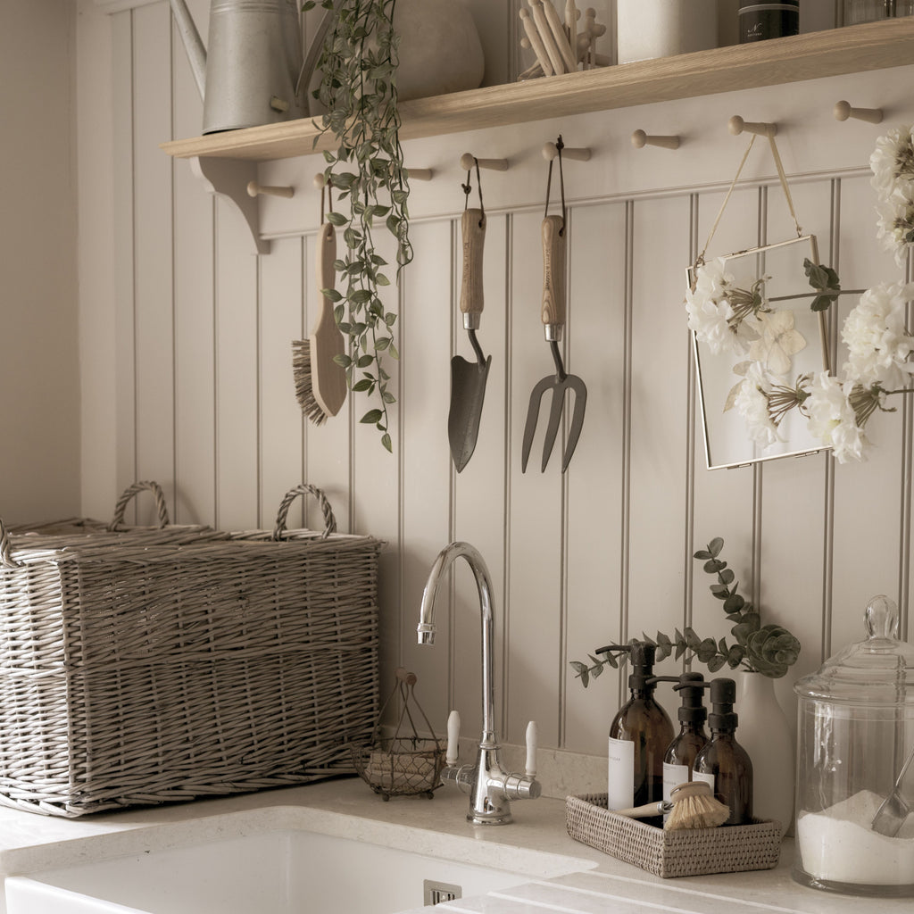 Neutral utility room with garden tools, wicker basket, glass jars, a sink, and eucalyptus plants.