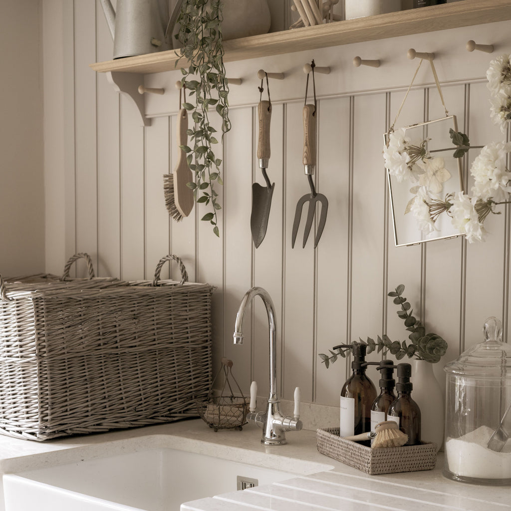 Neutral utility room with garden tools, wicker basket, glass jars, a sink, and eucalyptus plants.