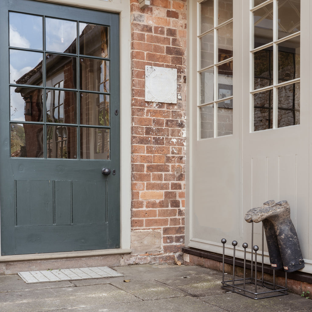 From The Anvil's Pewter boot rack with a pair of welly boots, outside a painted wooden door on a red brick property.