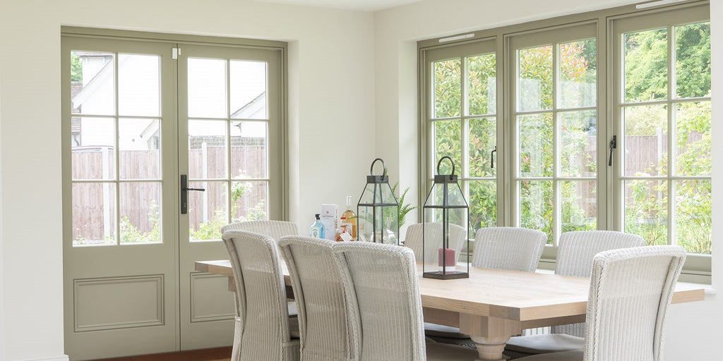 Modern sun room with a wooden dining table, white wicker chairs, and cream doors and windows with Pewter From The Anvil hardware.