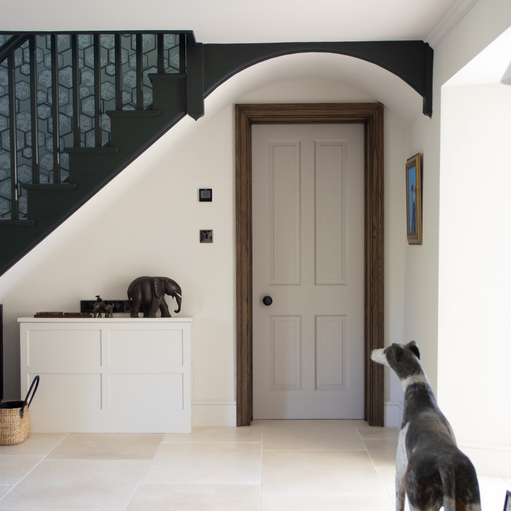 White wood panelled door with From The Anvil's Aged Bronze mortice door knob, underneath a painted staircase.