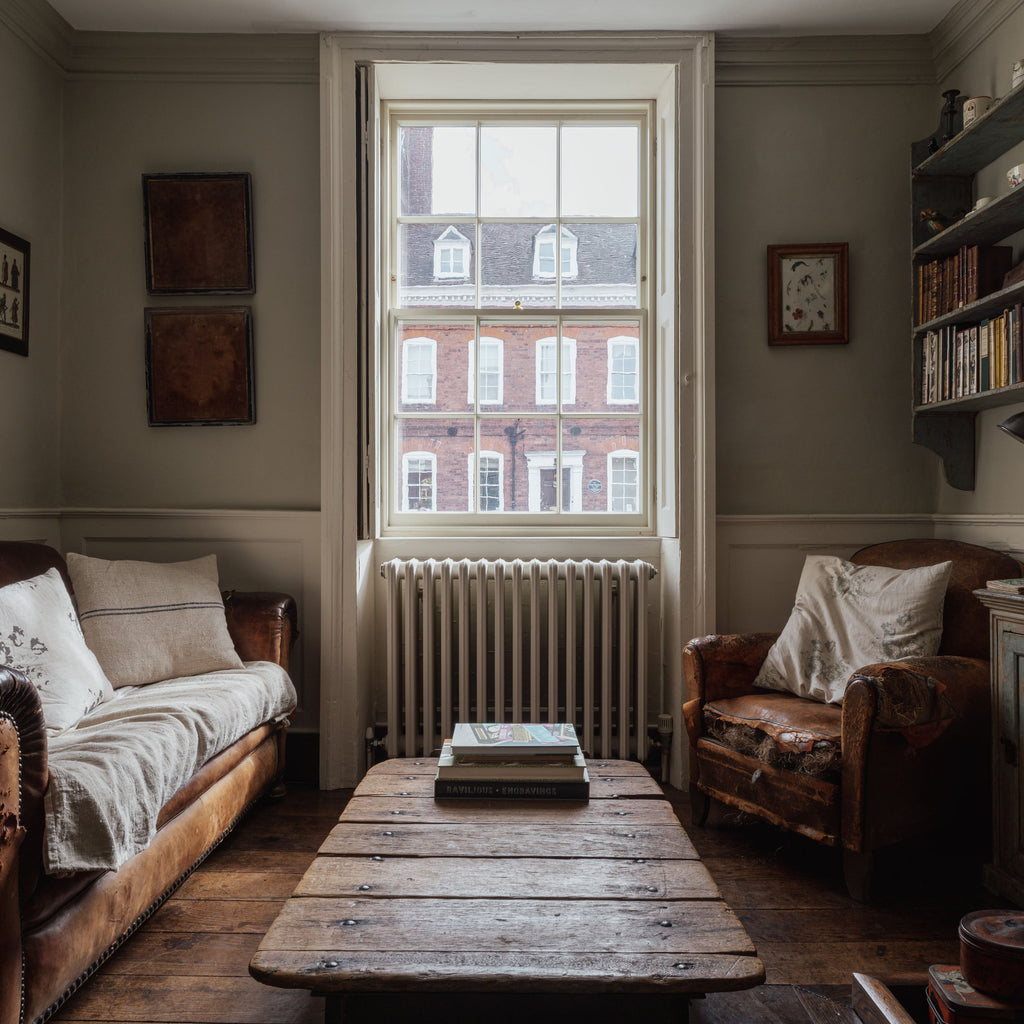 Period Property interior with vintage leather sofas, rustic wooden table, and white sash window.