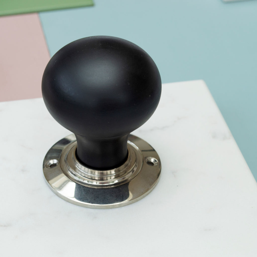 Close-up image of our Ebony round door handle with a Polished Nickel backplate on a piece of marble with green, pink and blue colours in the background.