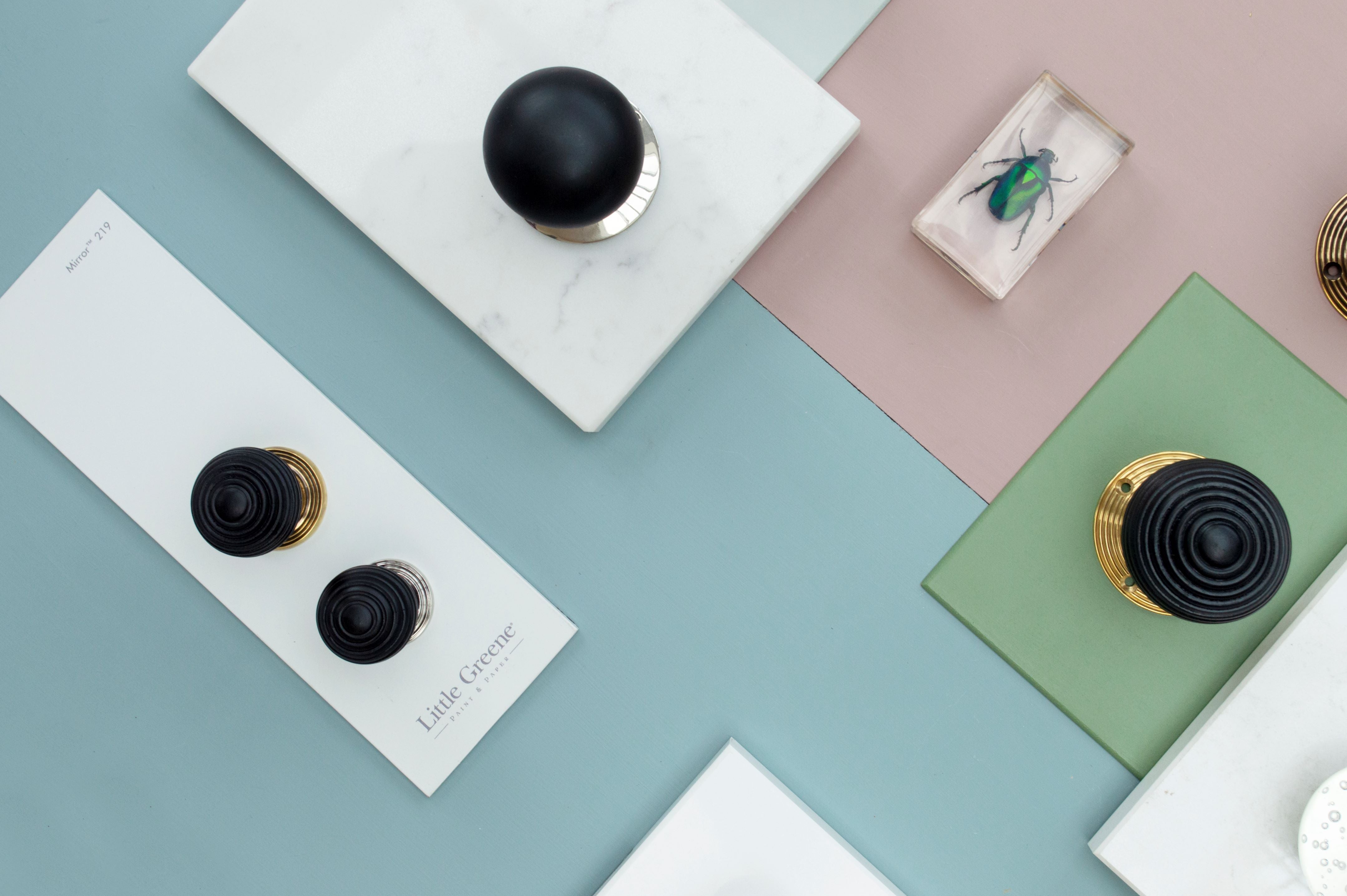 Ironmongery moodboard with pink, blue and green background, featuring Ebony cabinet knobs and door knobs among various props.