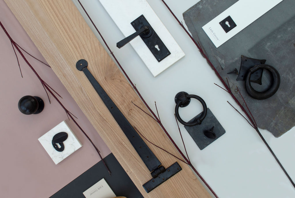 Ironmongery mood board with wood, marble, slate and pink backdrop, featuring External Beeswax T hinge, escutcheon, door knob, door knockers and lever door handles.
