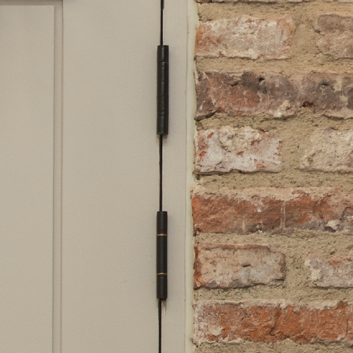 Closeup of a wood painted panelled door with Black butt hinges next to a brick wall.