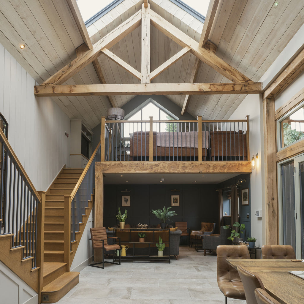 Modern barn conversion with oak beams, oak staircase, stone floors, and brown leather furniture in a bright interior.