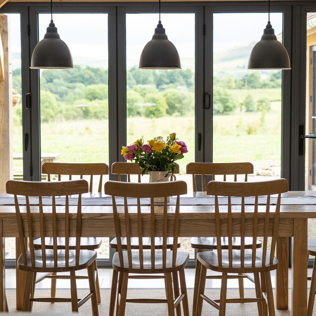 Dark grey From The Anvil Brindley pendant lights hung over a wooden dining table and chairs.