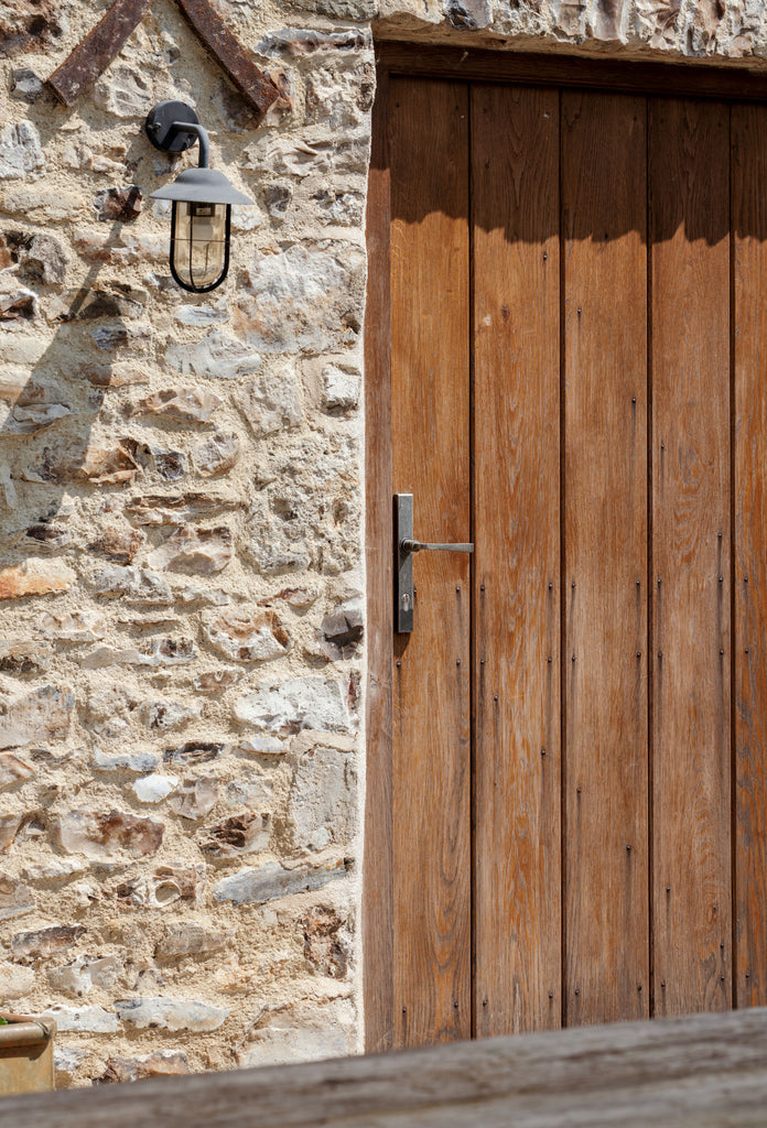 Weathered wooden door on a stone wall with From The Anvil's Pewter slimline lever lock door handle.
