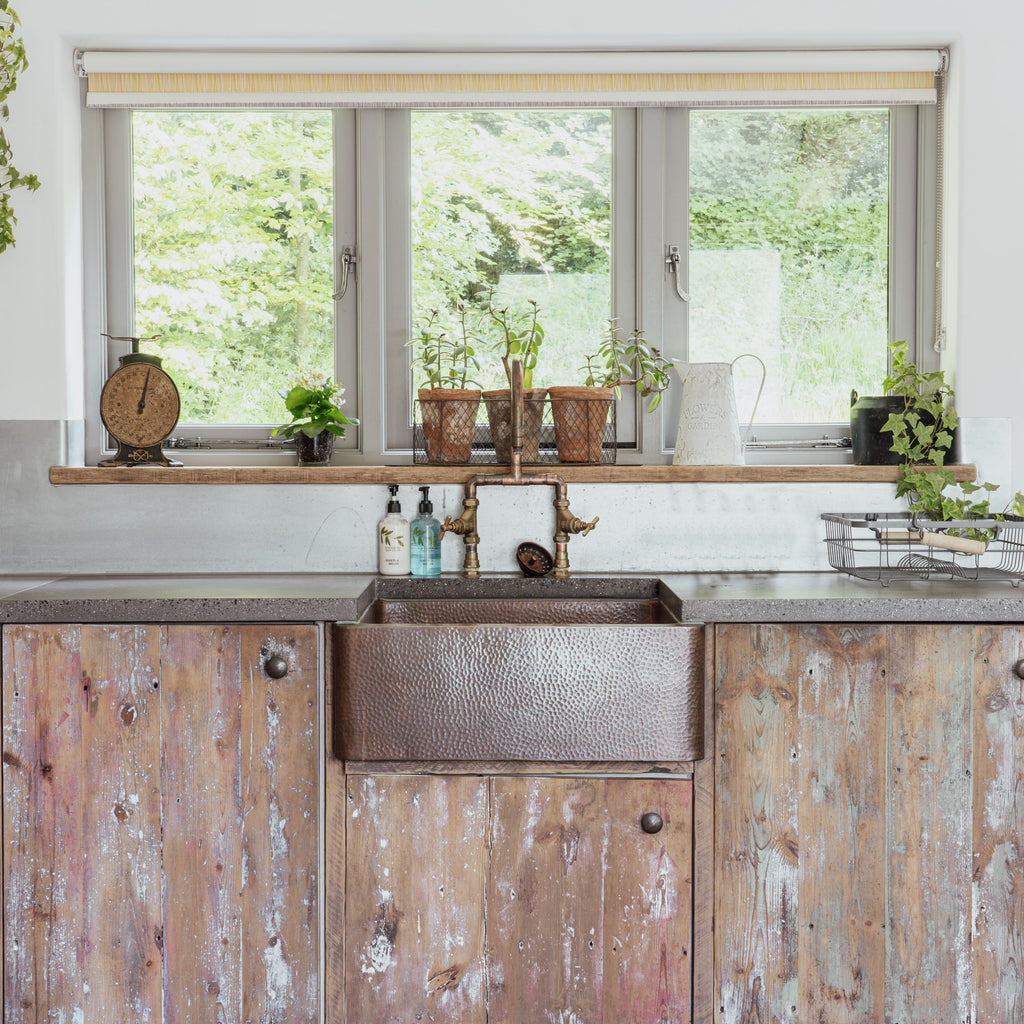 New Rustic kitchen interior with weathered wooden cupboards, hammered metal sink, and aluminium framed windows.