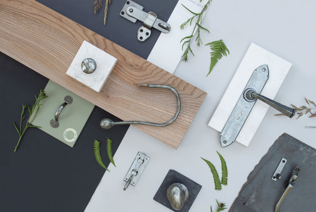 Ironmongery mood board with navy and white background, sheet of slate, plank of wood and Pewter door handle, cup hook, pull handle, cabinet knob and latch.