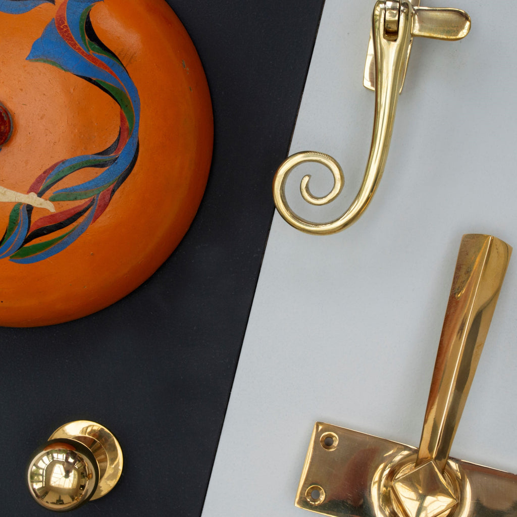 Polished Bronze cabinet knob, window fastener and door handle in a moodboard with a decorative orange pot.