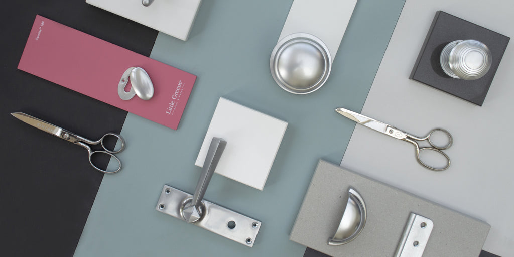 Satin Chrome mood board with pink, grey and blue backgrounds and Satin Chrome escutcheon, door handle, door knob, cabinet knob, pull handle and hinge and 2 pairs of scissors.