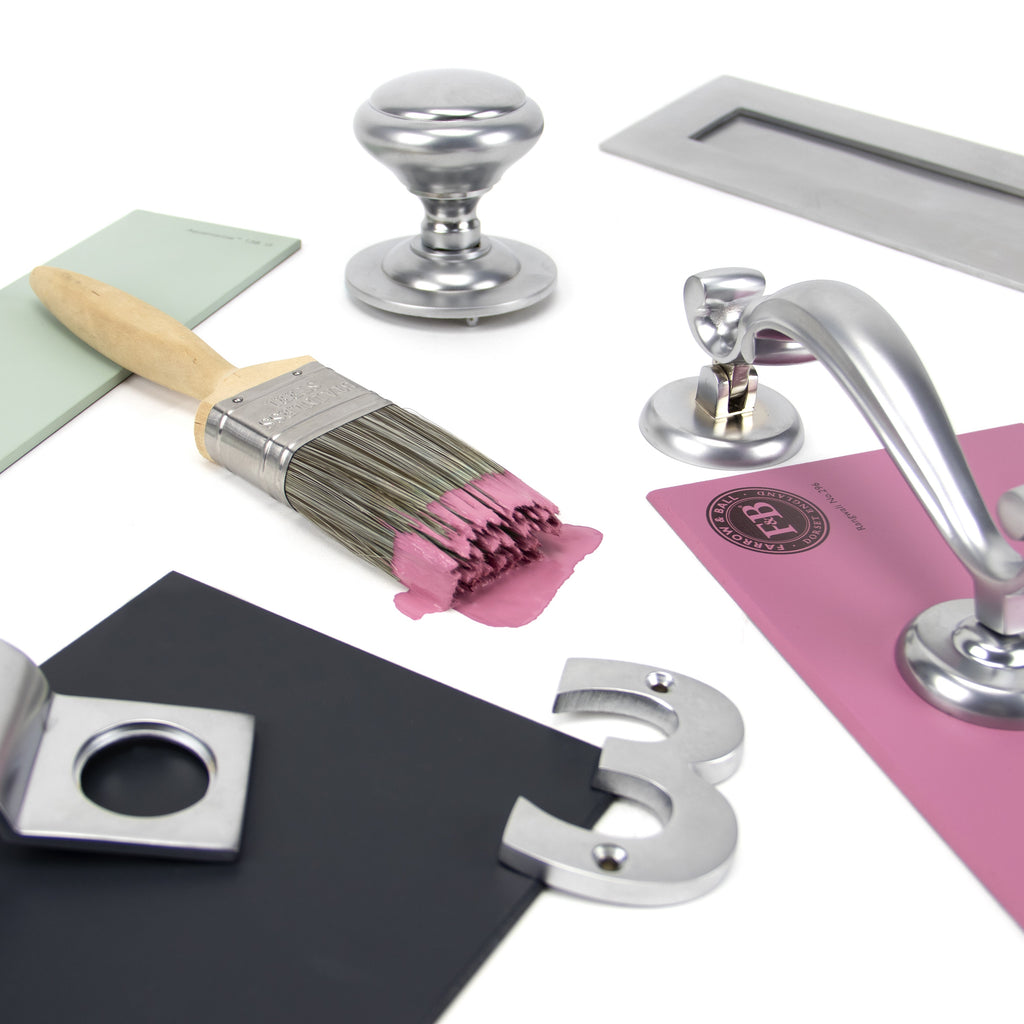 Ironmongery mood board with Satin Chrome ring pull, door knob, door knocker, letterplate, numeral 3, and pink, green and grey paint swatches with a wooden paint brush dipped in pink paint.